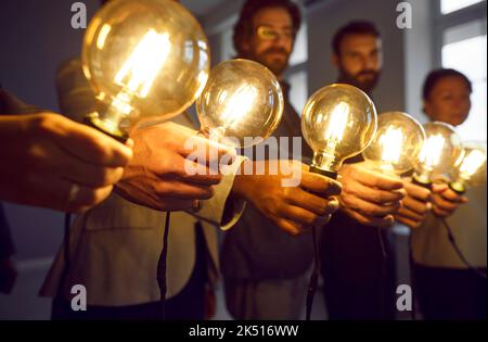 Glowing light bulbs in hands of creative business team in office as symbols of their ideas. Stock Photo