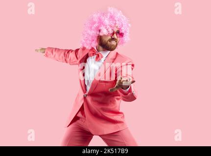 Funny bearded man in wig, glasses and suit having fun isolated on pink background. Stock Photo