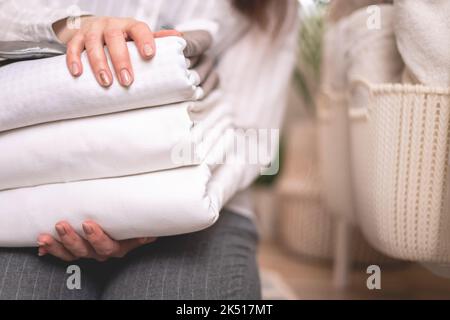 Beautiful woman in winter thick warm robe is sitting and neatly folding bed linens and bath towels Stock Photo