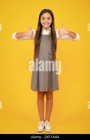 Like it. Portrait of joyful teenage child girl showing thumbs up and smiling, yellow background with copy space. Stock Photo