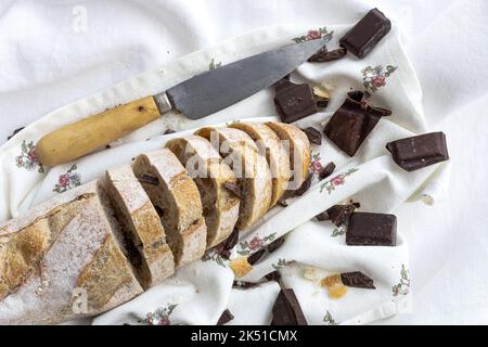 High angle of freshly baked cut bread loaf with chocolate bars and knife placed on white napkin on table in kitchen Stock Photo
