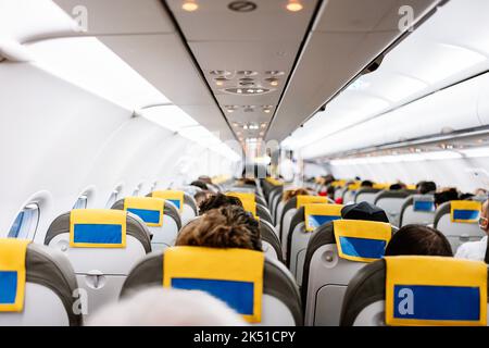 Unrecognizable passengers sitting on comfortable chairs under control panel inside contemporary aircraft during trip Stock Photo