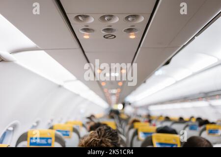 Unrecognizable passengers sitting on comfortable chairs under control panel inside contemporary aircraft during trip Stock Photo