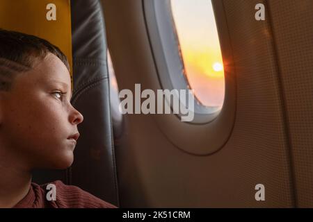 Side view of calm boy sitting on chair looking out the windows in plane Stock Photo