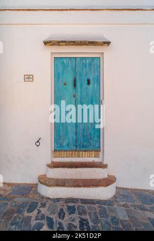 Exterior of aged stone building with shabby wooden door in turquoise paint and stone street pavement Stock Photo