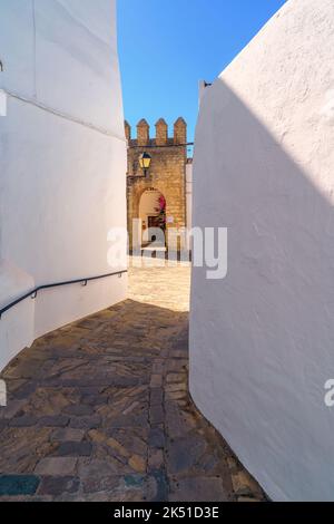 Old stone houses with white plaster walls and narrow walkway paved with stones leading to masonry fort building in sunlight Stock Photo