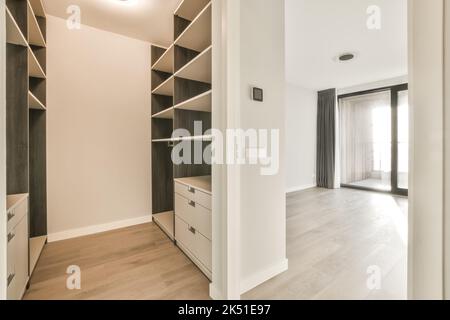 Empty dressing room with built in wooden wardrobe cases with shelves next to empty room Stock Photo