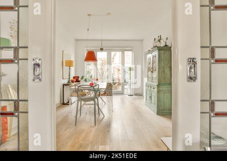Light room with wooden parquet floors and glass doorways furnished with wooden dining set and aged cupboard in daylight Stock Photo