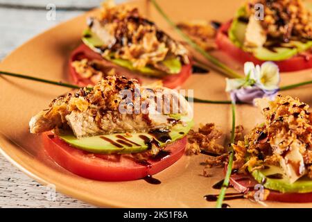 Closeup crispy fried onion and sliced of mackerel placed on slices of tomato and avocado near greens and flowers on plate in restaurant Stock Photo