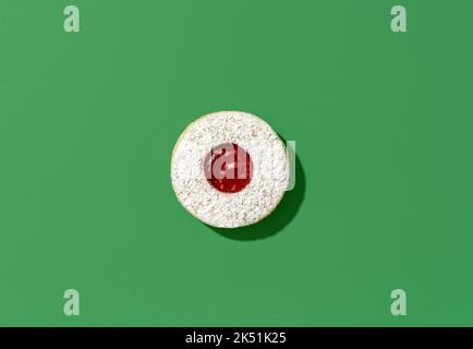Above view with a linzer cookie minimalist on a green table. Traditional christmas dessert, german recipe, cookie filled with jam. Stock Photo