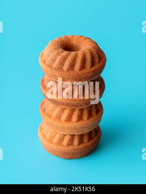 Close-up with a stack of mini bundt cakes, minimalist on a blue table. Tiny sponge cakes stacked one above each other on a blue background. Stock Photo