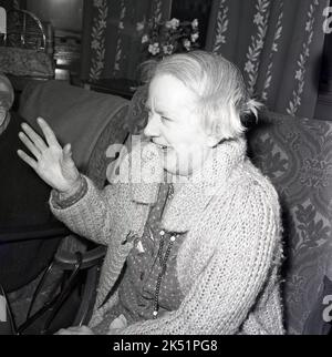 1964, historical, a sprightly elderly lady wearing a big cotton cardigan has a laugh sitting in her chair in an old peoples home, Stock Photo