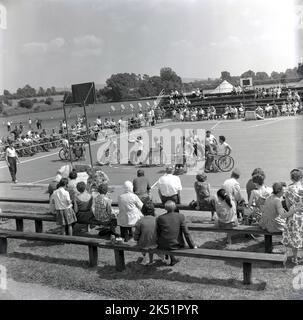1964, in the grounds of Stoke Mandeville Hospital, home of the National Spinal Injuries Centre - established in 1944 by Dr. Ludwig Guttmann-spectators watch wheelchair athletes compete in a basketball tournament. Stoke Mandeville in Aylesbury, Buckinghamshire, England, UK, was the birthplace of the Paralympic movement on 29th July 1948, the opening ceremony of the post-war London Olympics. On this day, the first competition for wheelchair athletes took place when 16 injured serviceman and women competed in an archery event in what was known as the Stoke Mandeville Games. Stock Photo