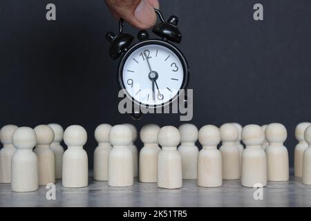 Working hours, hourly wages, deadline concept. Alarm clock and wooden dolls on black background. Stock Photo