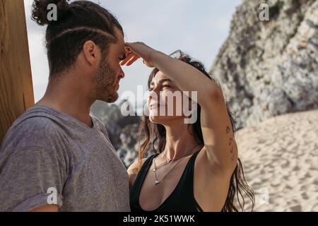 tattooed woman touching face of bearded boyfriend on beach in portugal,stock image Stock Photo