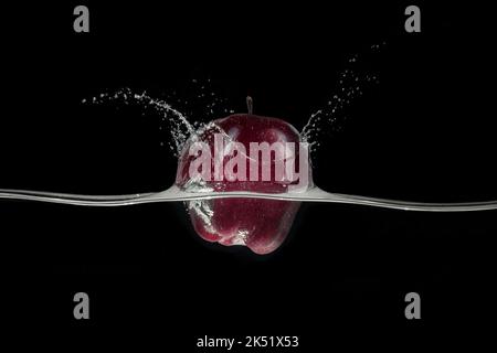 Red apple splashing in water, viewed from a side on black background. Stock Photo