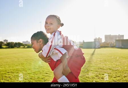 Girl soccer and team friends on field enjoying match game leisure break with fun piggyback ride. Happy, young and excited football children relax Stock Photo