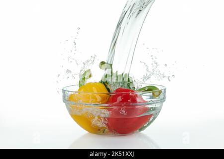 waterfall pouring onto a glass bowl with multicolored peppers with splashes on white background. Stock Photo