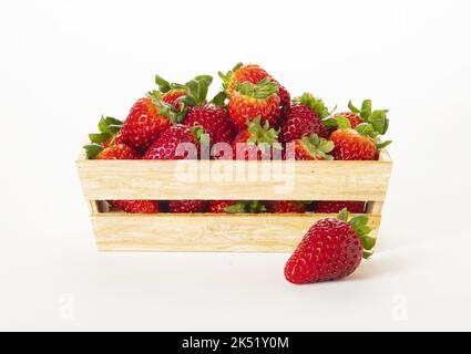 Wooden basket full of strawberries with one out on the surface. On White background. Stock Photo