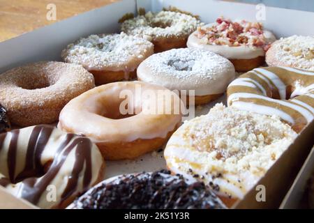 Picture of assorted donuts in a box with chocolate frosted, glazed, and Bacon donuts. Stock Photo