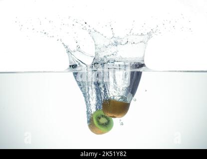 Two half kiwi splashing in water forming crown splash. On white background. Stock Photo