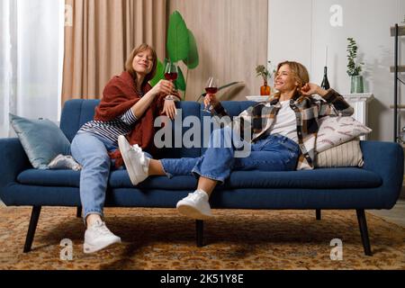 Mother and daughter relaxing on a couch talking while drinking wine Stock Photo