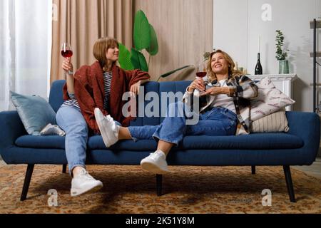 Mother and daughter are gossiping while drinking wine while sitting on the couch at home Stock Photo