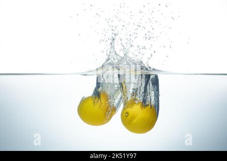 Two lemons splashing in clear water. Side view on white background. Stock Photo