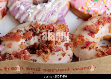 Picture of assorted donuts in a box with Bacon topping, pink glazed, and sprinkles donuts. Stock Photo