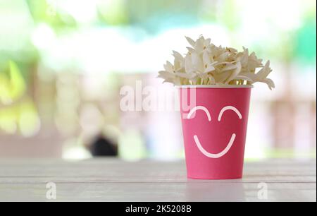 Pink paper cup with a smile symbol and white flowers blooming on top cup and have copy space for design in your work. Stock Photo