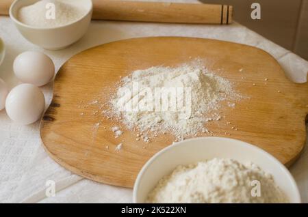 Baking ingredients. Board, apple, eggs, flour,  rolling pin and eggshells on the kitchen table. Baking concept. Process of making homemade pie. Series Stock Photo