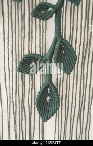 green leaf branch handmade macrame artistic wall hanging fiber art decoration leaf symbol wood stick white background interior plant macramé deco Stock Photo