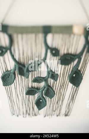 green leaf branch handmade macrame artistic wall hanging fiber art decoration leaf symbol wood stick white background interior plant macramé deco Stock Photo