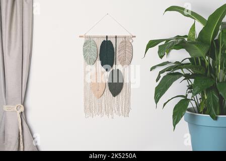 macrame handmade artistic wall hanging fiber art decoration leaf feather symbols wood stick interior plant macramé nature green forest olive beige Stock Photo