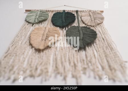 macrame handmade artistic wall hanging fiber art decoration leaf feather symbols wood stick interior plant macramé nature green forest olive beige Stock Photo