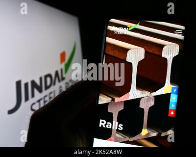 Person holding cellphone with webpage of company Jindal Steel and Power Limited (JSPL) on screen with logo. Focus on center of phone display. Stock Photo
