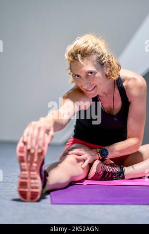 Real young mature caucasian woman in a sport wear at gym doing stretching workout at gym. Fitness concept. Stock Photo