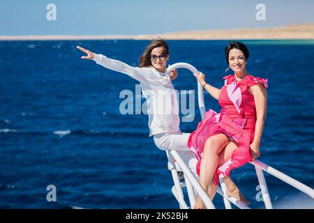Two women relaxing together on the nose of the yacht at sunny summer day at sea Stock Photo