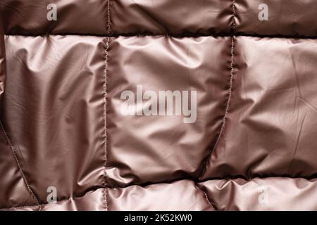 womens quilted bronze brown padded jacket as background, background of soft light fabric of a padded jacket, winter padded jacket Stock Photo