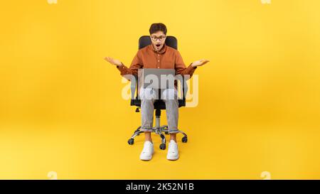 Shocked Man Using Laptop Working Online Sitting On Yellow Background Stock Photo