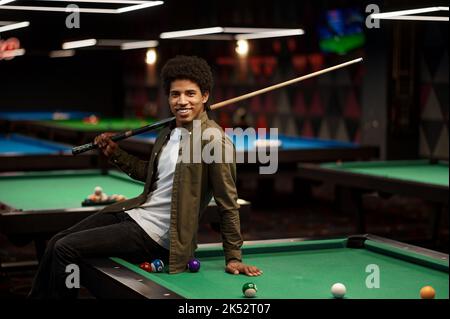 Young pool player with cue sitting on billiard table Stock Photo