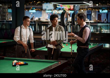 Company of handsome young guy playing in pool Stock Photo
