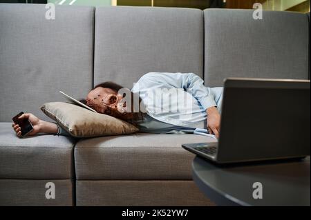 Overworked zombie sleeping on sofa in office Stock Photo