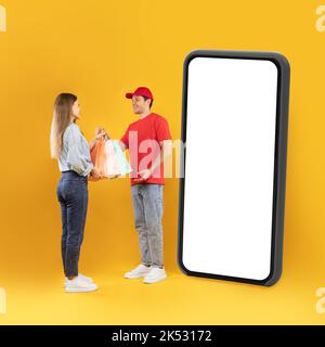 Deliveryman Giving Bags To Woman Standing Near Large Cellphone, Studio Stock Photo