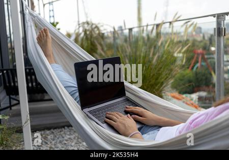 young woman freelancer working in hammock on terrace Stock Photo