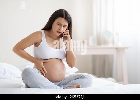 Upset pregnant woman feeling some pain and discomfort, calling doctor Stock Photo