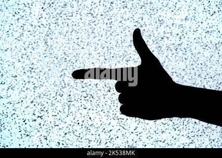 Man doing the finger guns gesture, fingers making a gun symbol, hand black silhouette isolated on TV screen, noise, closeup. Gestures, gesturing abstr Stock Photo