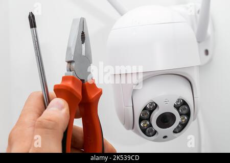 Technician installing CCTV camera using pliers and screwdriver outside of the building. Stock Photo