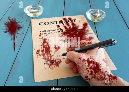 Bloodied man's hand and with fountain pen, signing a demonic contract next to lit candles. Stock Photo