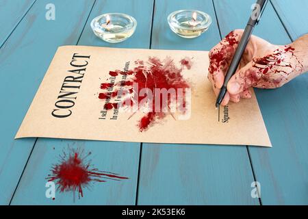 Bloodied man's hand and with fountain pen, signing a demonic contract next to lit candles side view. Stock Photo